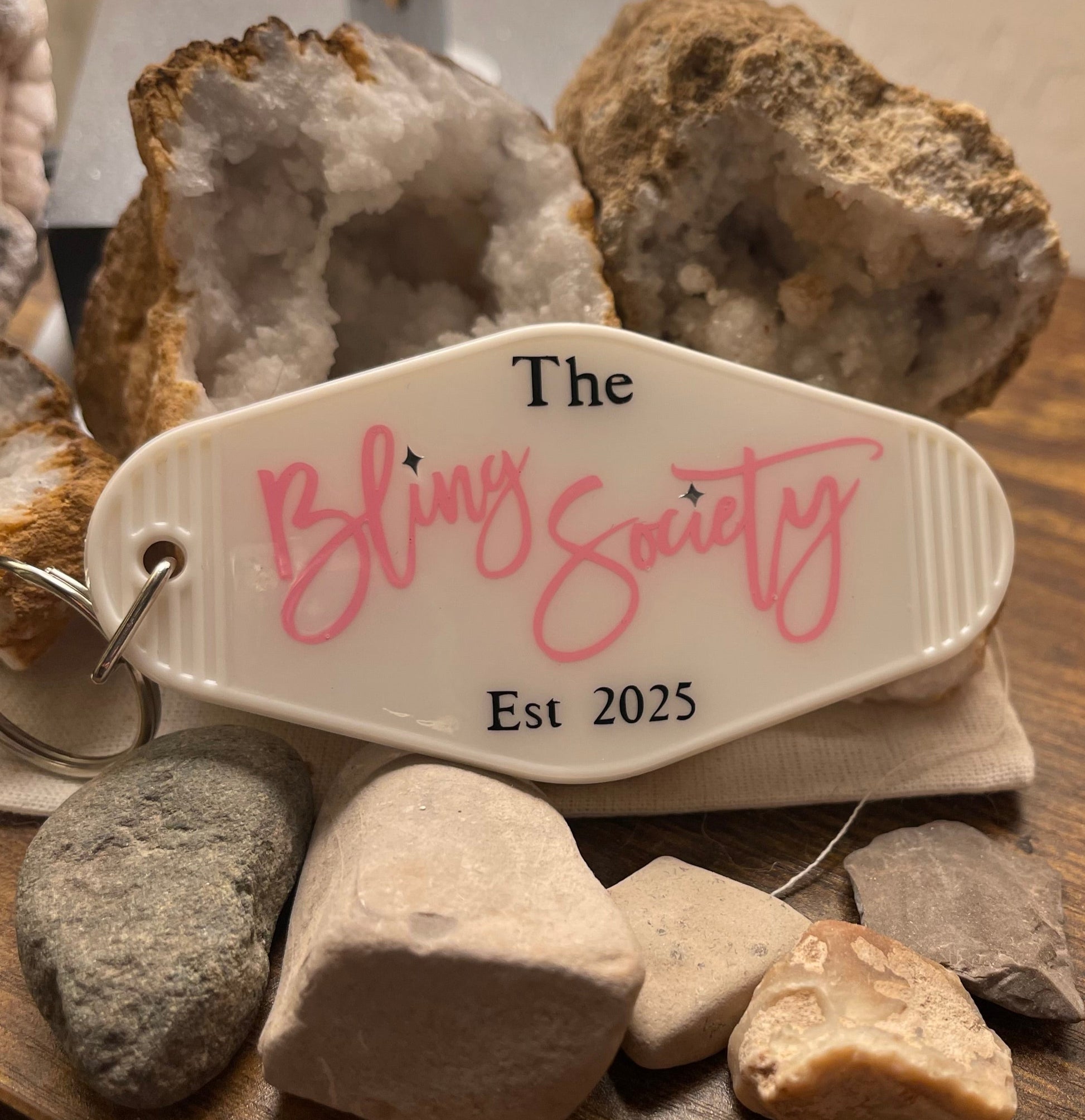 Keychain with 'The Bling Society' logo on a wooden surface with rocks